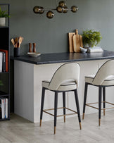 Stylish bar stools with cream upholstery and black legs, paired with a sleek black countertop and modern pendant lighting.