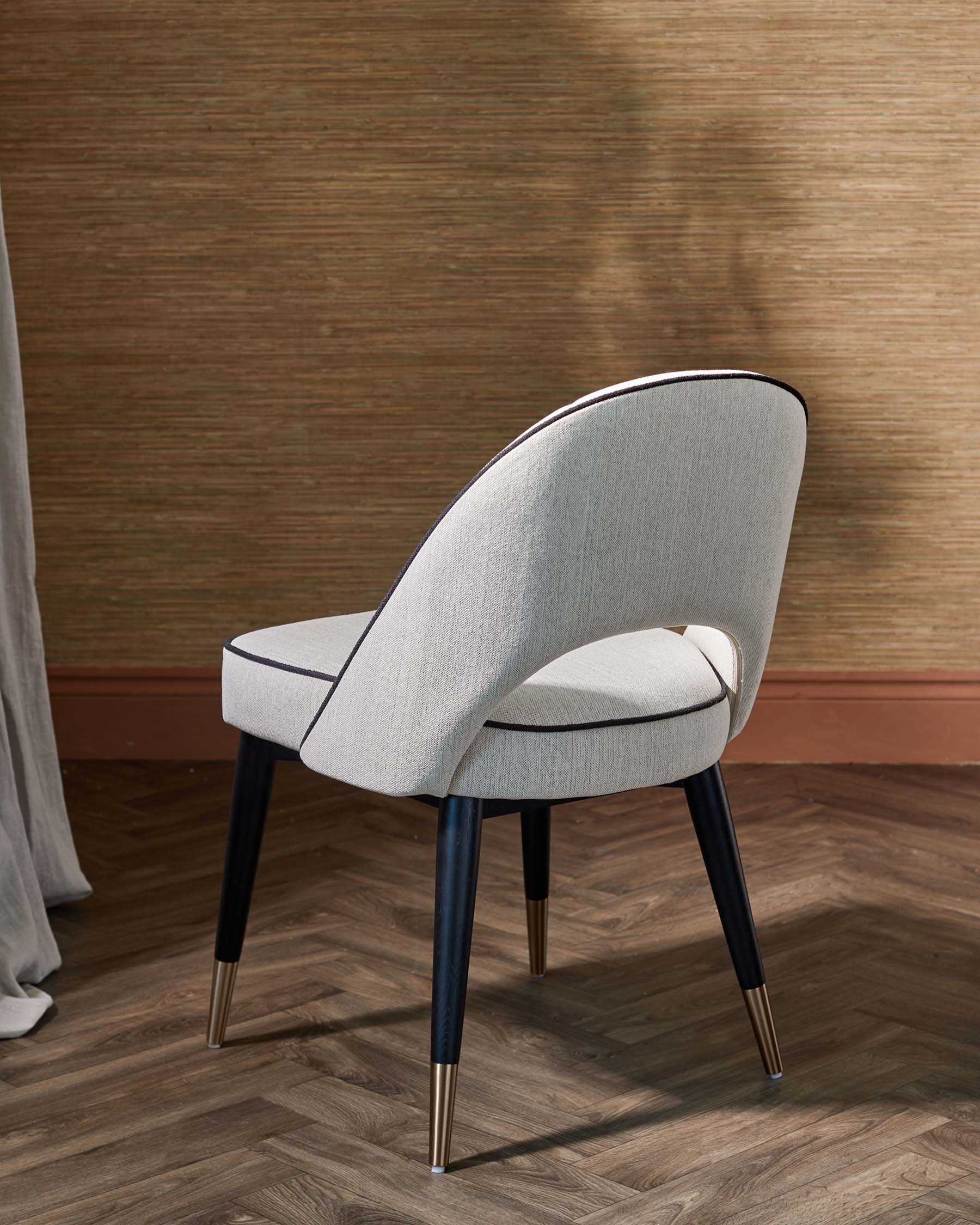 Elegant gray chair with black legs and gold accents, featuring a curved backrest and plush seat, set against a textured backdrop.