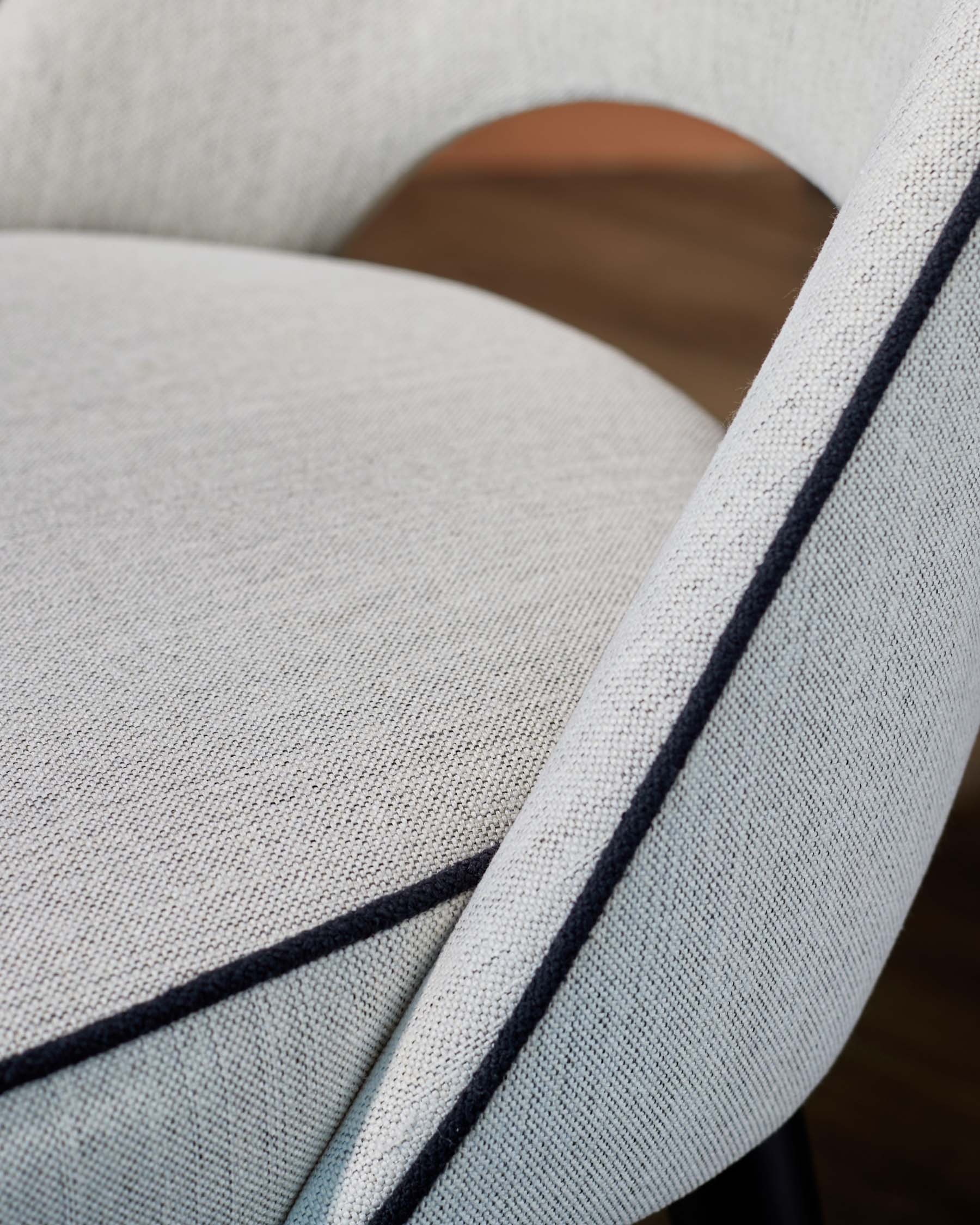 Stylish chair with light gray fabric, featuring a textured finish and contrasting dark stitching along the edges.