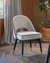 Sleek gray upholstered chair with a curved back, dark legs, and gold accents, set against a warm-toned wall and natural decor.