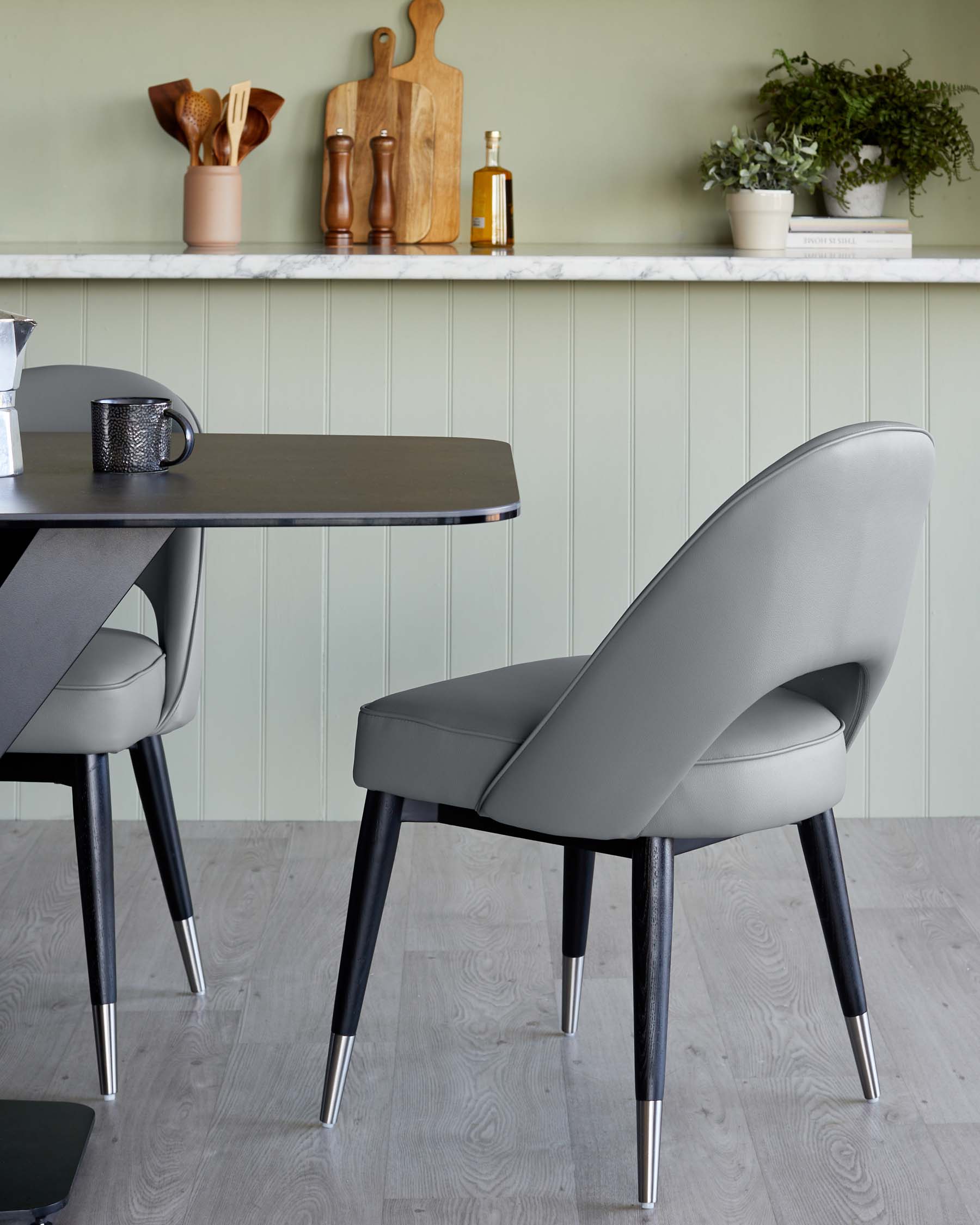 Elegant modern dining set featuring a round black table with a sleek tabletop and angled metal legs, paired with a sophisticated light grey upholstered dining chair with a curved backrest and tapered black legs with metallic tips.