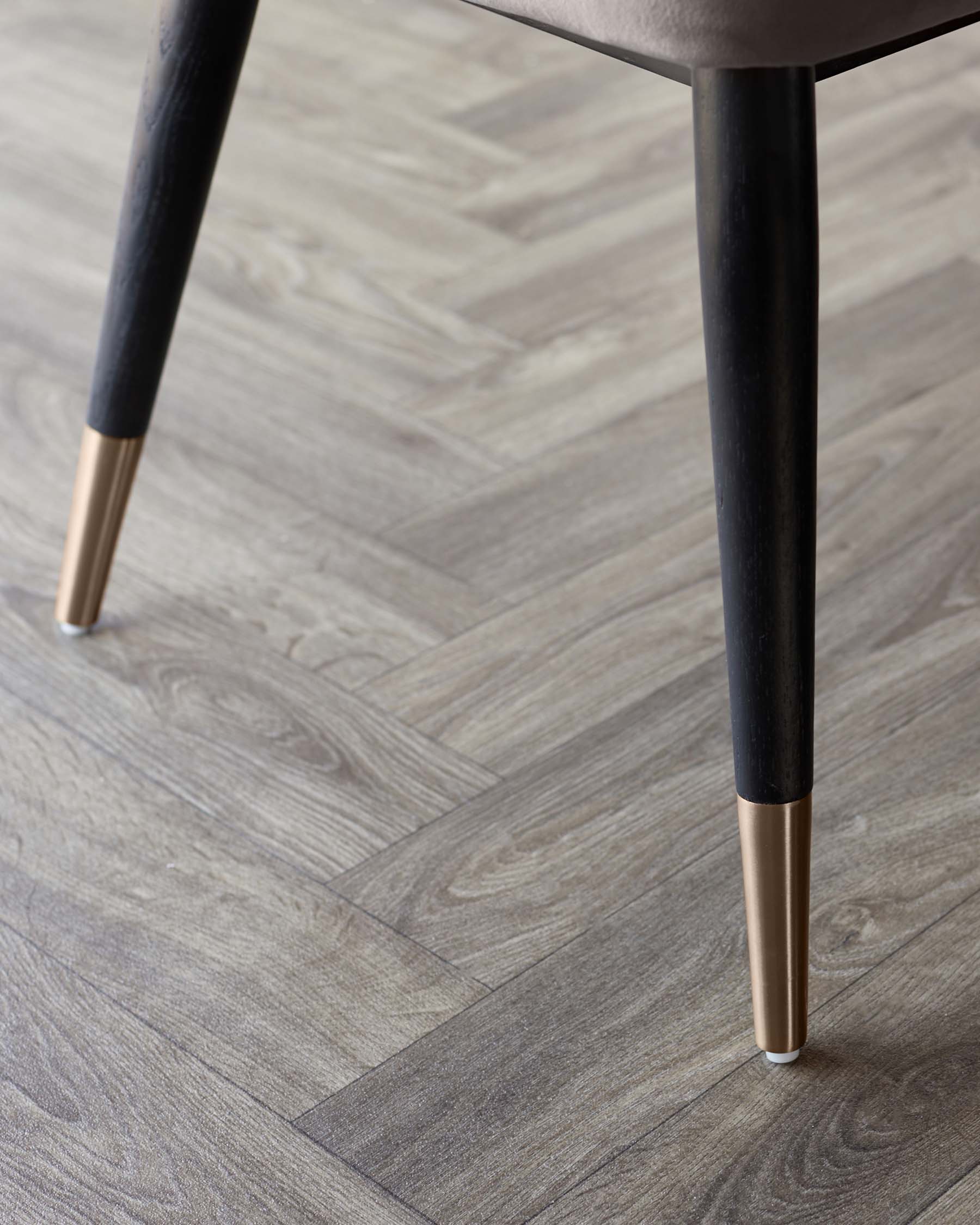 Close-up of modern chair legs with black finish and gold accents, resting on a textured wooden floor.