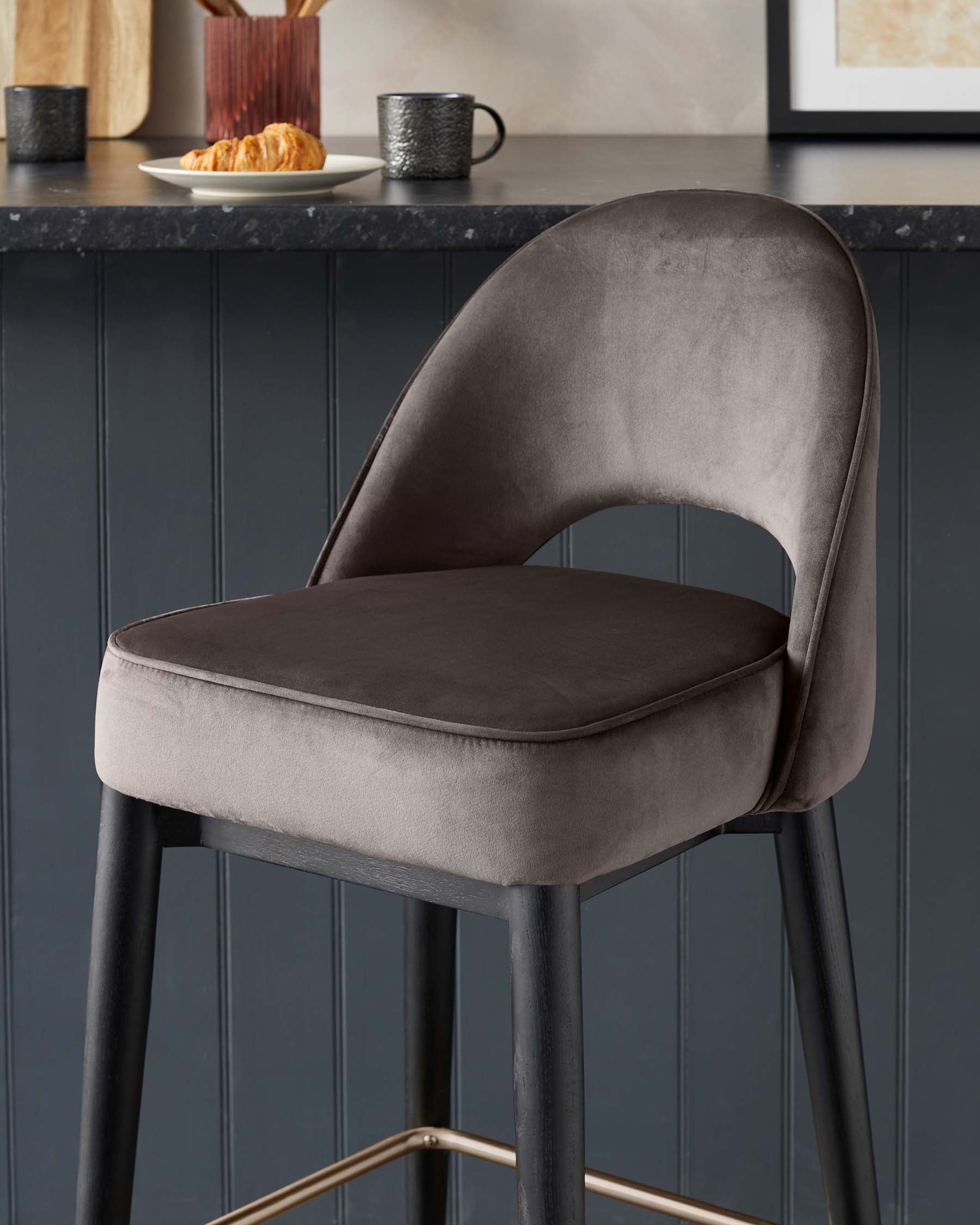 Modern velvet upholstered bar stool with a curved backrest and sleek black metal legs featuring gold accents on the footrest.