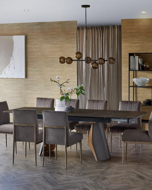 Modern dining set featuring a sleek, dark table with an artistic base and plush, grey upholstered chairs with gold accents.