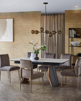 Modern dining set featuring a sleek table with unique base and plush, upholstered chairs with metal accents.