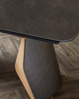 A modern table featuring a textured dark top and a unique, sculptural wooden base in contrasting shades.