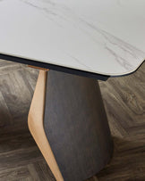 A sleek dining table featuring a marble top and a unique base combining dark wood and a light leather accent.