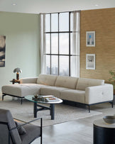 Modern sectional sofa in light beige with a minimalist design and dark tapered legs, paired with a round glass-top coffee table featuring a unique blue and black base, on a light grey area rug.