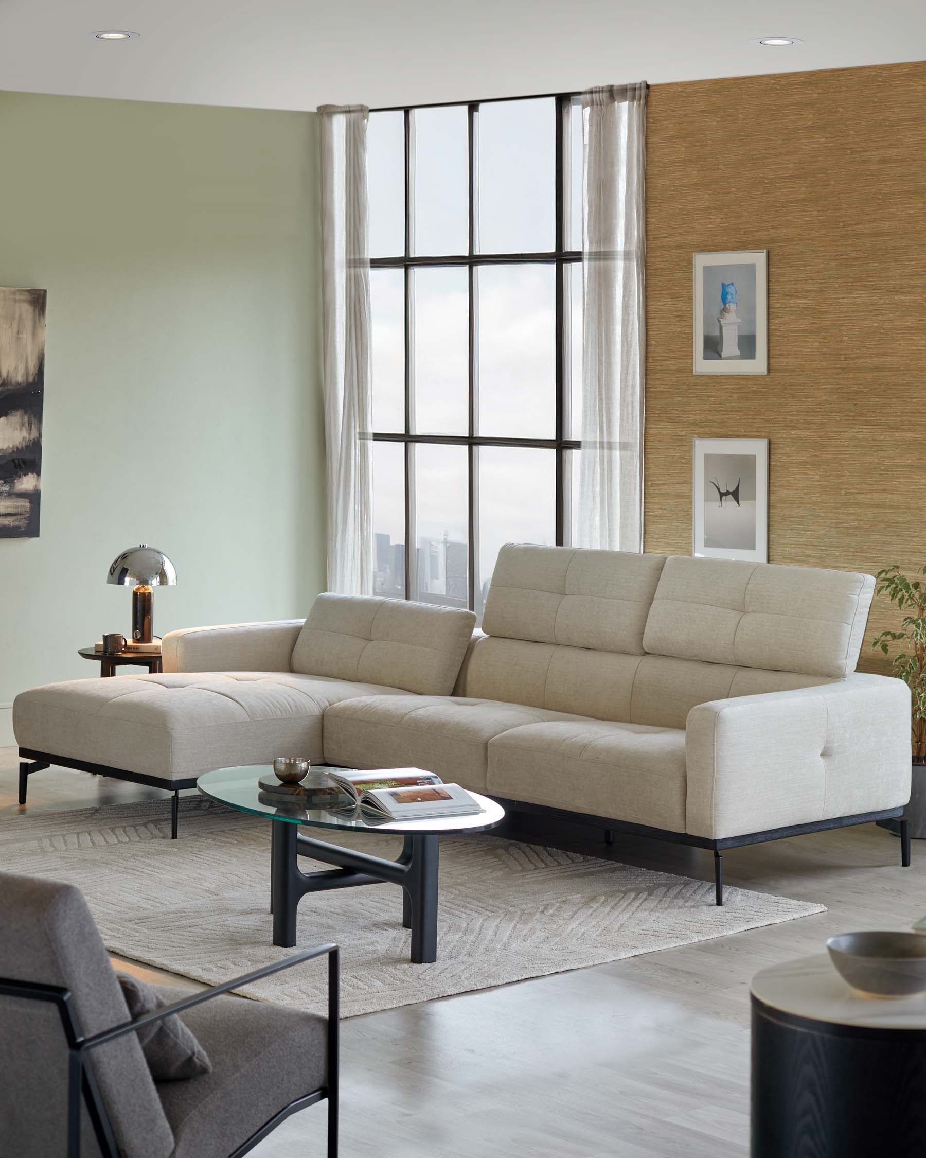 Modern L-shaped sectional sofa in a neutral beige fabric with square tufting, complemented by a round glass-top coffee table with a unique grey frame, set atop a textured light grey area rug.