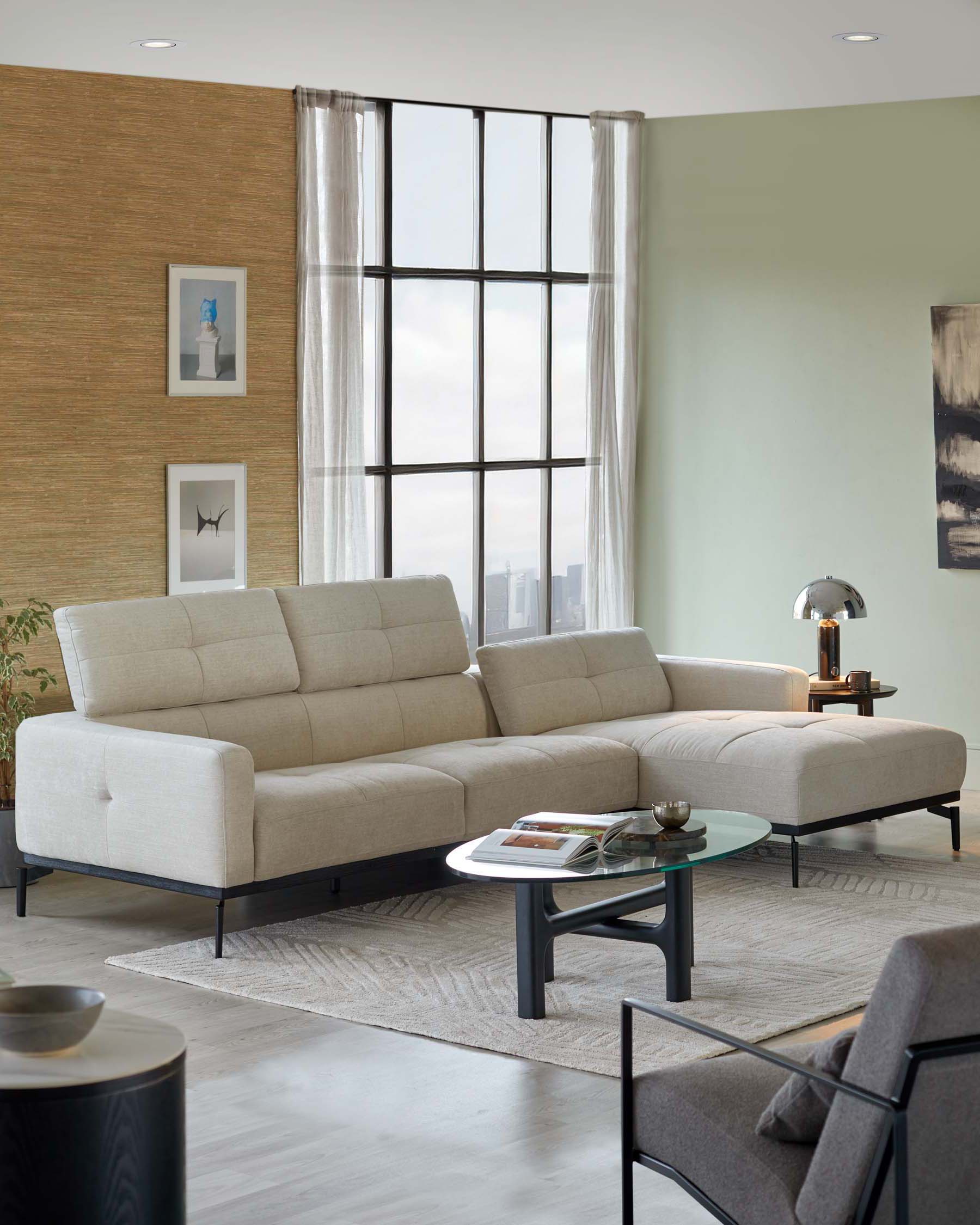 Contemporary light beige sectional sofa with clean lines and a minimalist design; placed on a textured grey area rug with a matte black round coffee table that has a glass top and unique intersecting leg structure. Nearby is a contrasting dark-toned side chair with slender, angled legs and armrests.