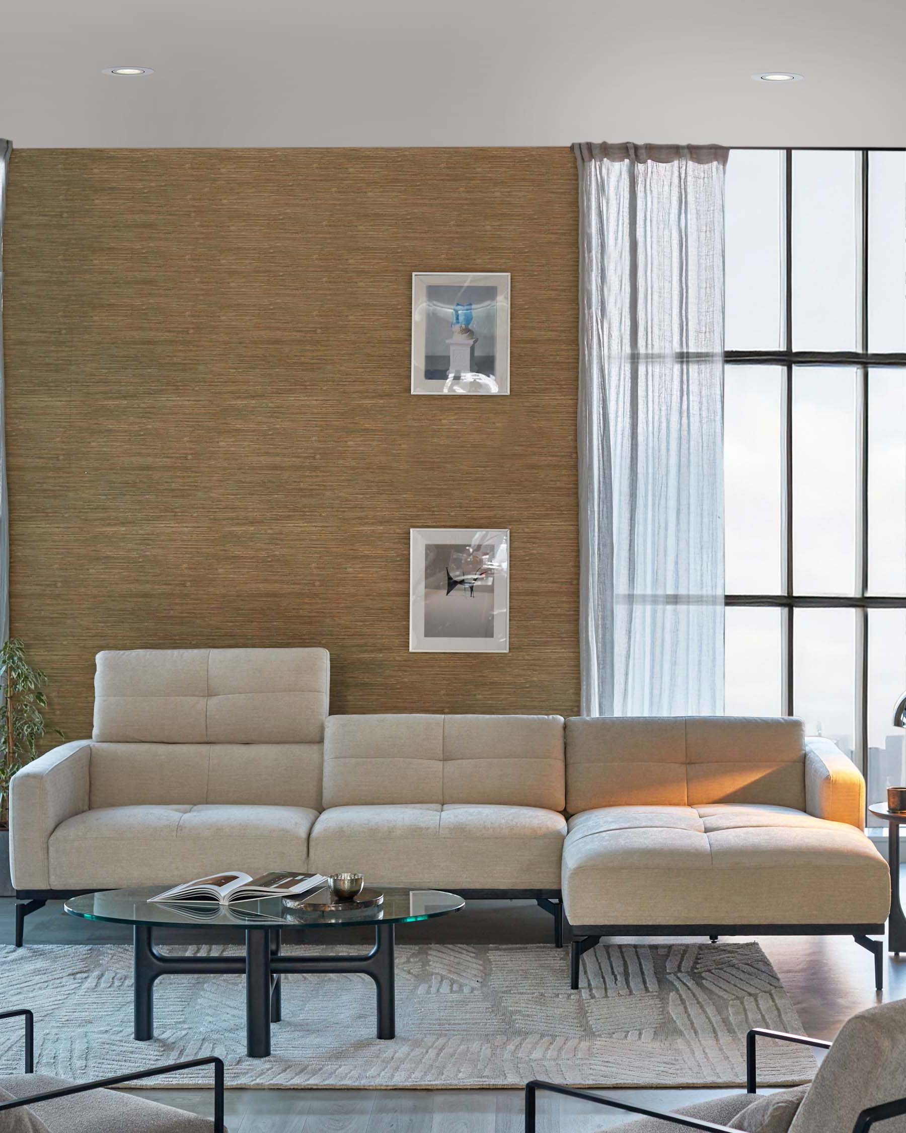 Modern beige L-shaped sectional sofa with clean lines and slim cushioned back, paired with a round glass-top coffee table with a black frame residing on a textured neutral area rug.