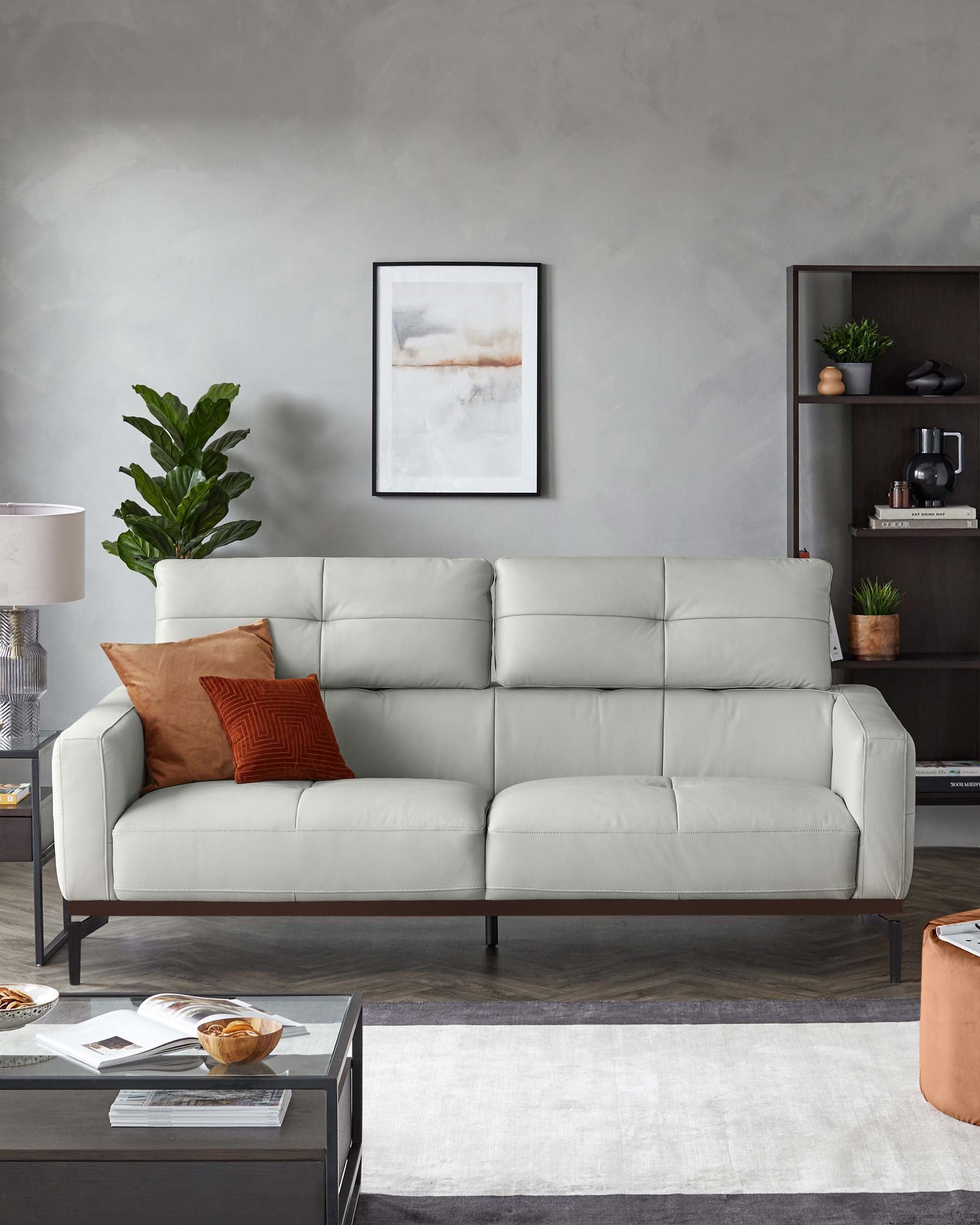 Modern light grey upholstered three-seater sofa with a minimalist design and dark, slim metal legs. On the right, a dark wooden bookshelf with simple lines and open shelving displaying decorative items. In the foreground, a rectangular coffee table with a dark finish and a lower shelf for additional storage, atop a two-tone grey area rug.