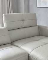 Modern light grey leather sectional sofa with clean lines and a plush backrest, featuring deep padded seats, situated in a well-lit room with soft grey curtains in the background.