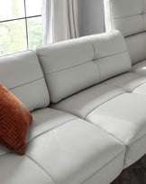 A modern light grey leather sectional sofa with a minimalist design, featuring clean lines, wide cushioned seats, and a slightly reclined backrest. A textured burnt-orange throw pillow adds a pop of colour to the neutral palette.