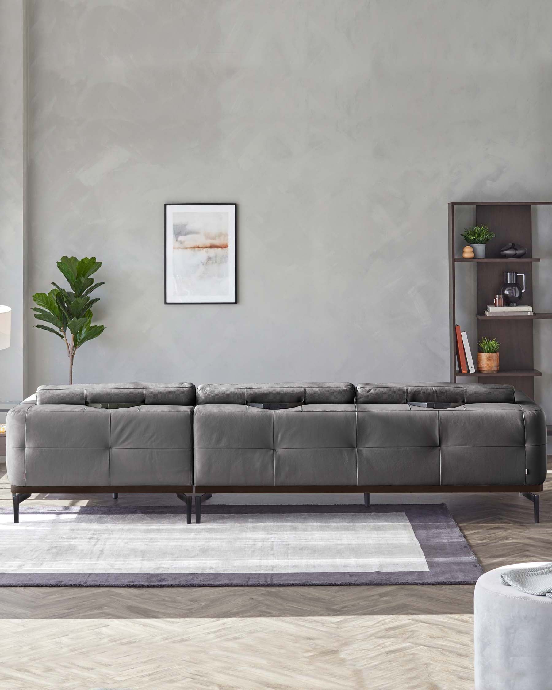 A contemporary grey tufted leather sectional sofa set on a two-tone patterned area rug, complemented by a modern shelving unit in the background displaying decorative items. A framed abstract artwork adorns the wall above, enhancing the room's minimalist sophistication.