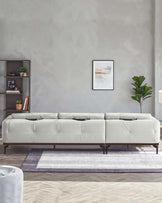 Modern light grey modular sectional sofa on a minimalist dark and light grey area rug, complemented by a dark wood shelving unit and green indoor plants.