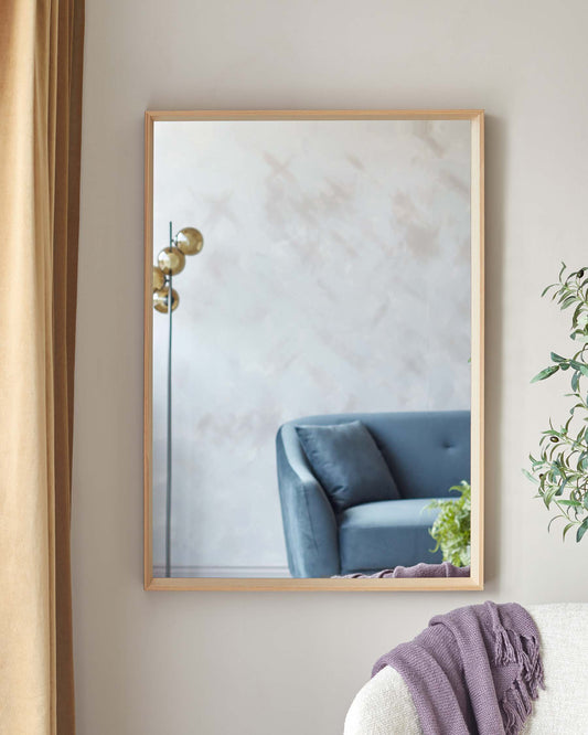 A sleek modern blue upholstered armchair with a high back and armrests reflected in a large square mirror with a light wood frame.