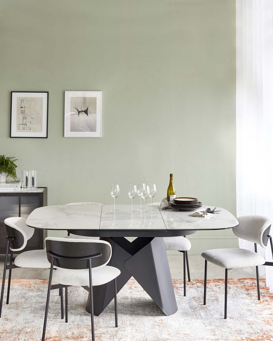 Modern dining table with marble top and black base, accompanied by stylish gray upholstered chairs, set on a patterned rug.