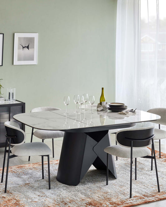 Modern dining table with a marble top and black geometric base, surrounded by comfortable light gray upholstered chairs.