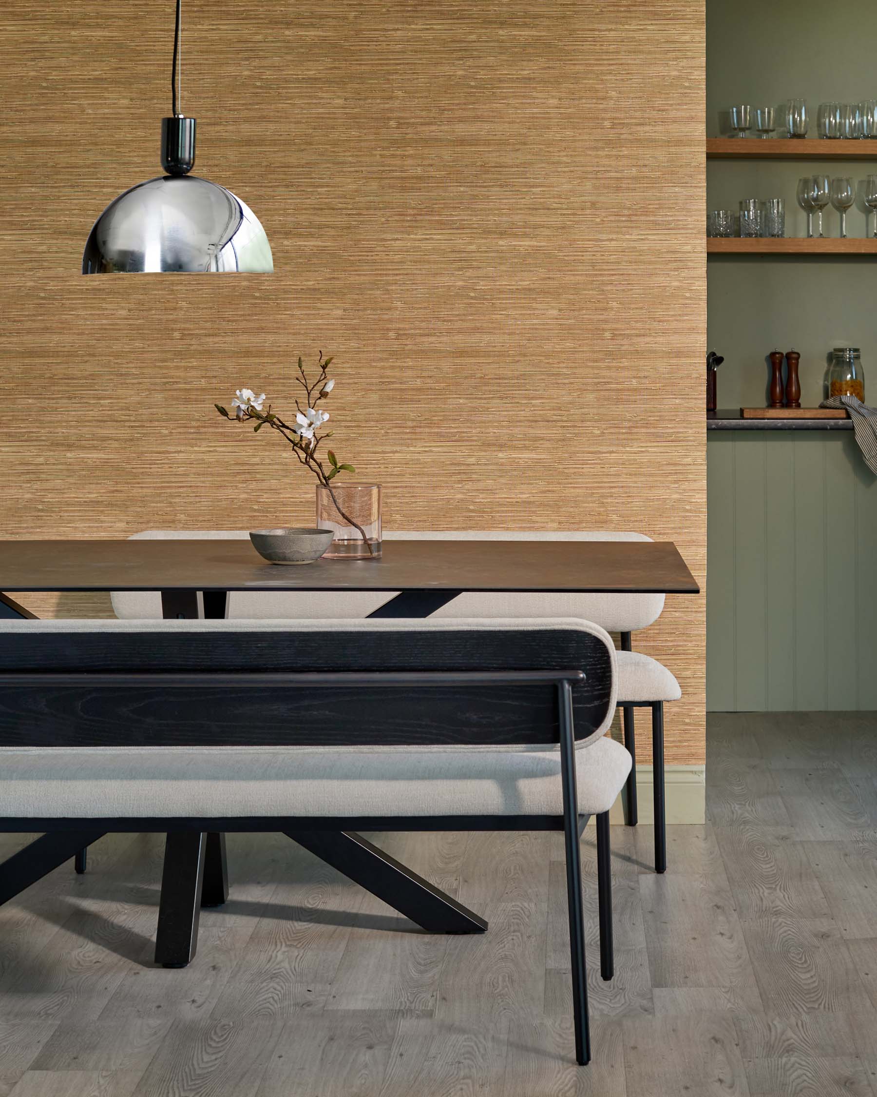 Stylish dining table with black legs, complemented by upholstered benches. Decorative vase and pendant light add elegance.