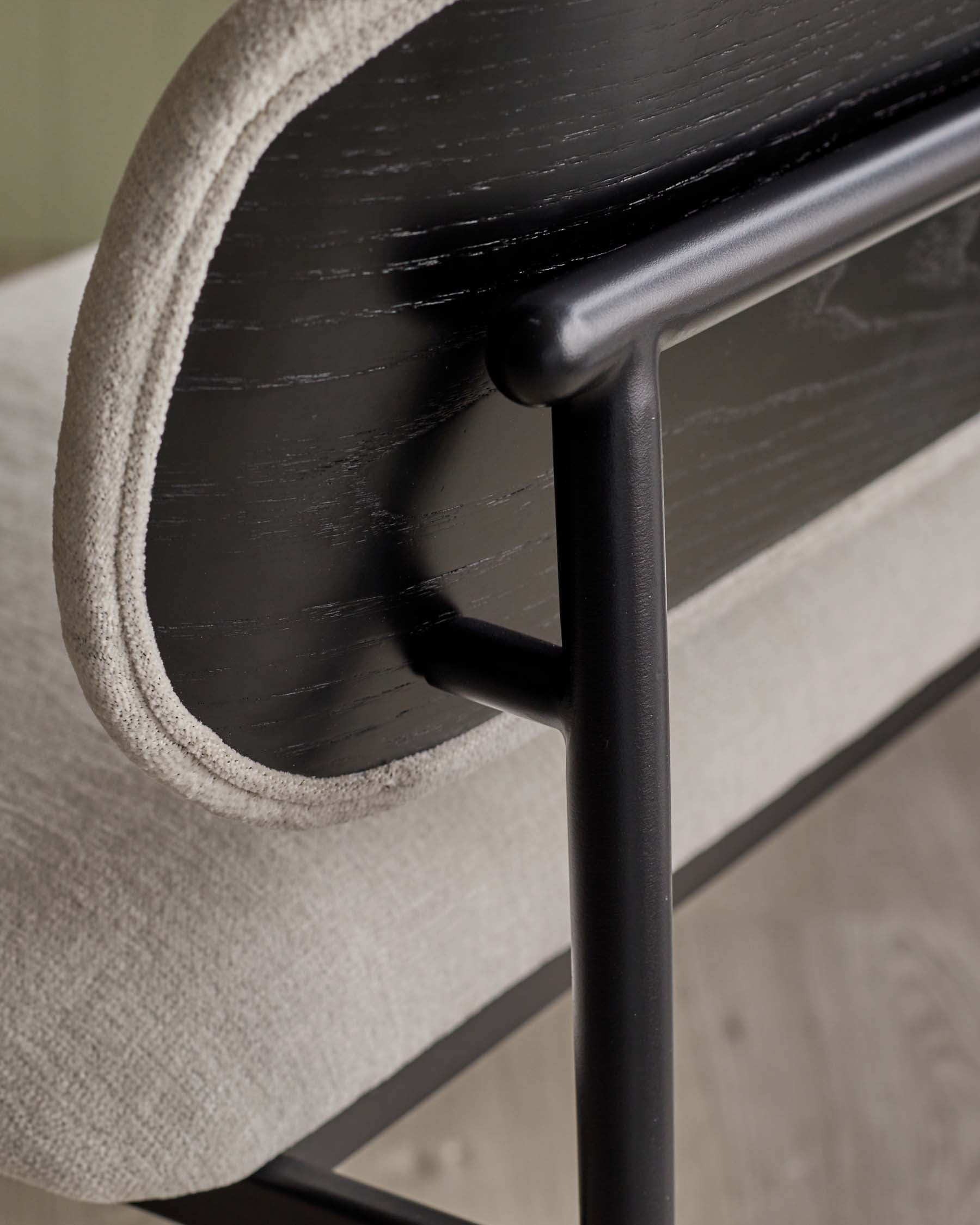 A modern chair featuring a sleek black wooden backrest, soft textured light fabric seat, and minimalist metal frame.