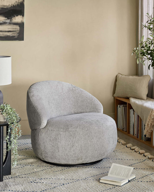 A cozy, rounded gray swivel chair, a side table with a lamp, a soft rug, and a decorative pillow on a wooden bench.