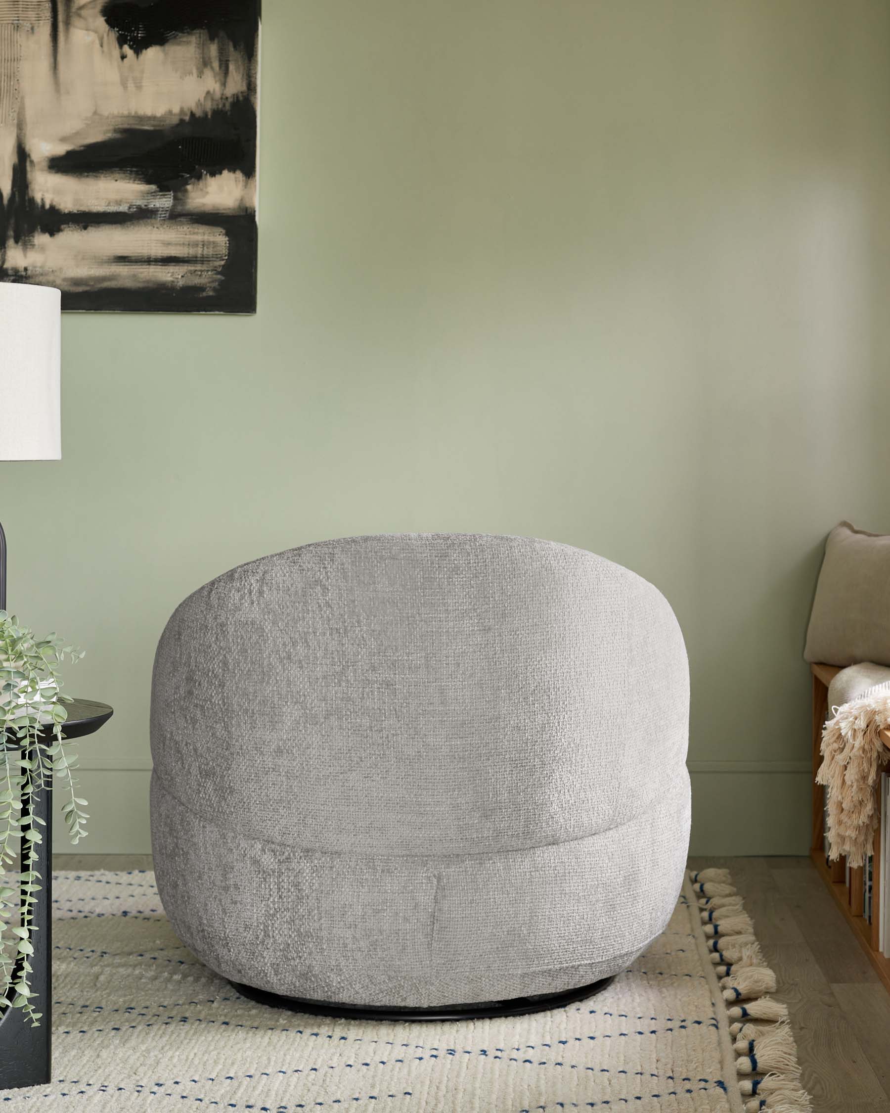 Round contemporary light grey upholstered ottoman with a textured fabric finish, placed on a beige and blue striped area rug with tassel details.