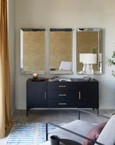 A sleek black sideboard with gold handles, three mirrors above, a decorative lamp, and a cozy gray sofa with accent pillows.