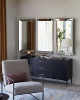 Modern furniture including a gray accent chair, a sleek dark sideboard with gold handles, and three framed mirrors above it.