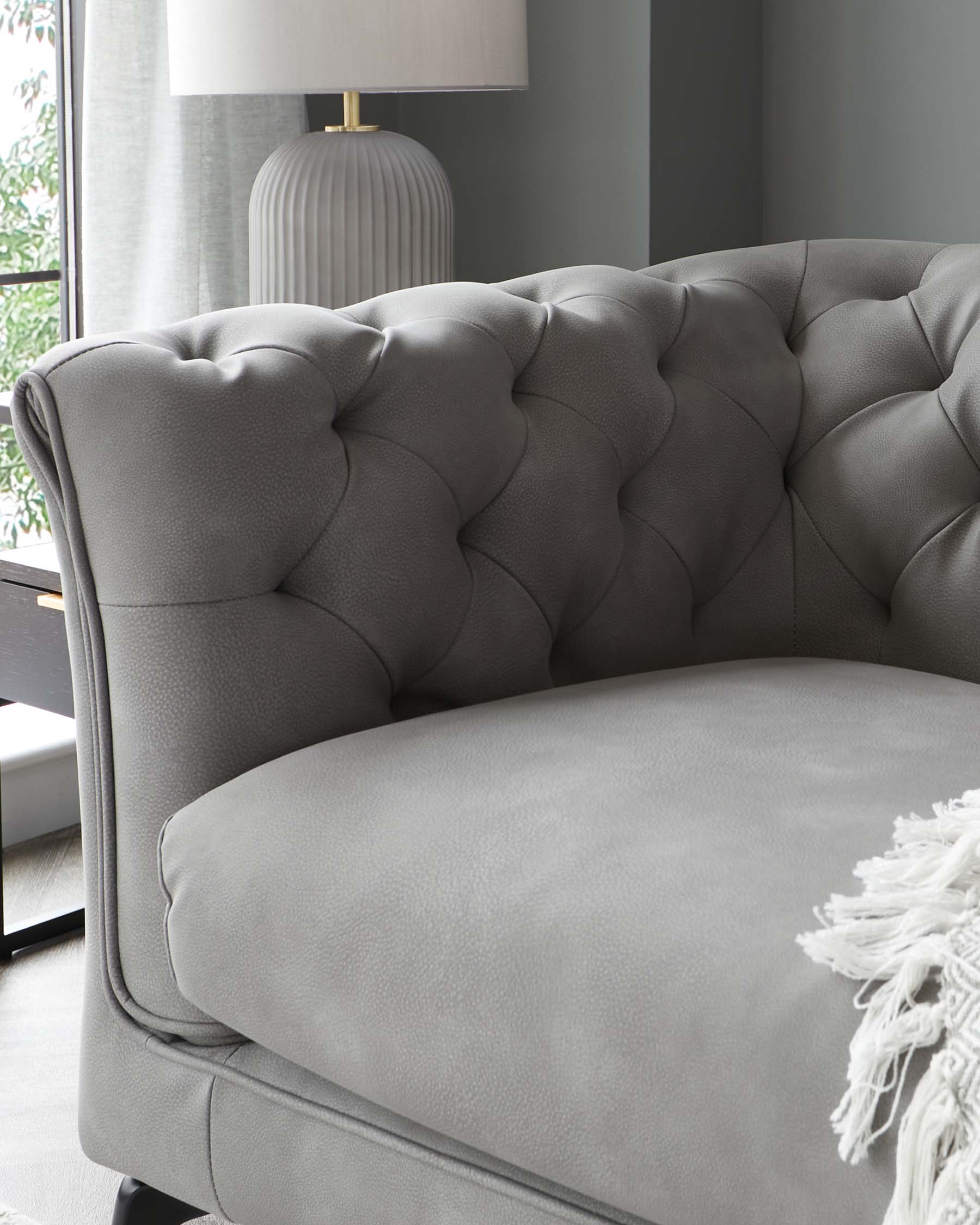 Stylish gray tufted sofa with plush cushions, complemented by a chic lamp and modern decor elements.