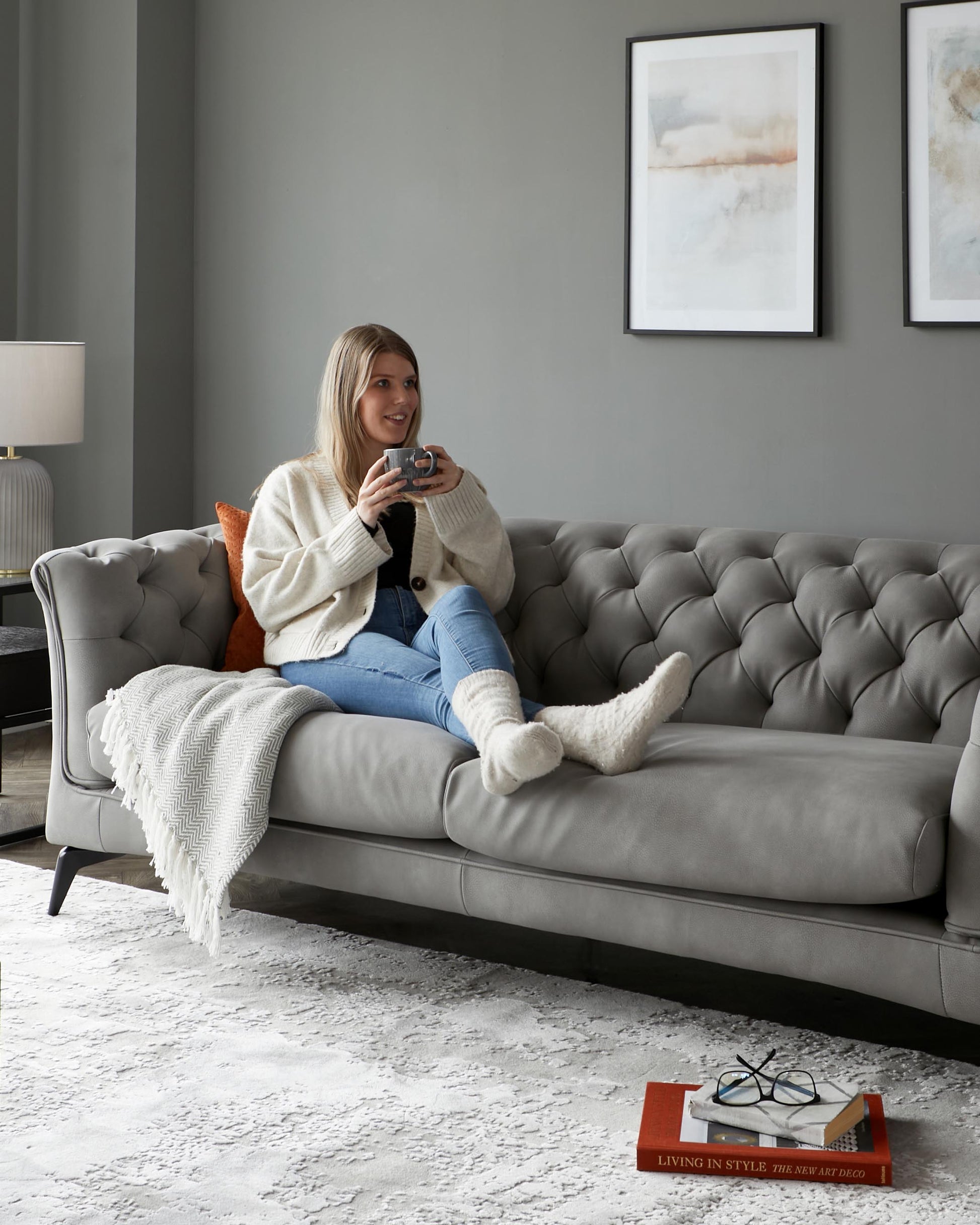 Chesterfield-style gray sofa with button tufting, cozy throw blanket, and decorative pillows, accompanied by a stylish side lamp.