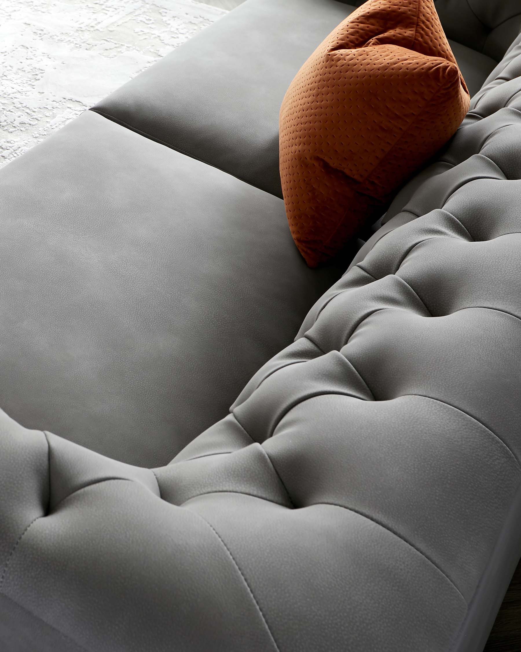 Elegant gray tufted sofa with a plush texture, complemented by a warm-toned decorative pillow.