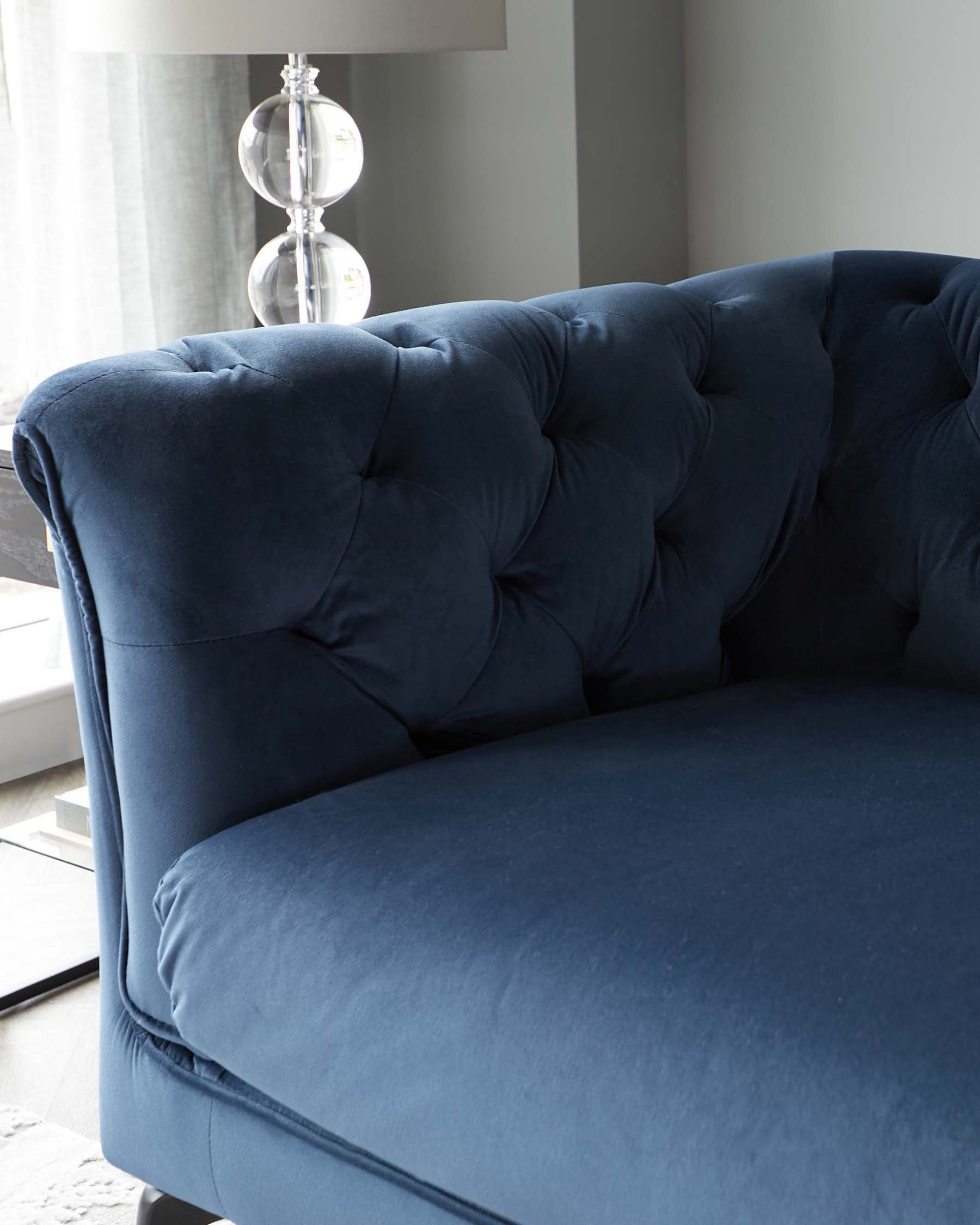 Elegant navy blue sofa with tufted upholstery, offering a modern touch. Accompanied by a stylish clear glass table lamp.