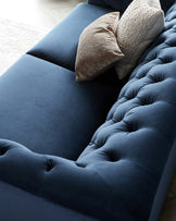 Luxurious navy velvet sofa with tufted details and two decorative pillows in contrasting textures.