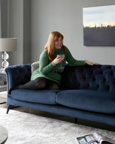 A tufted navy blue sofa with slender legs, complemented by a decorative lamp and an abstract wall art piece.