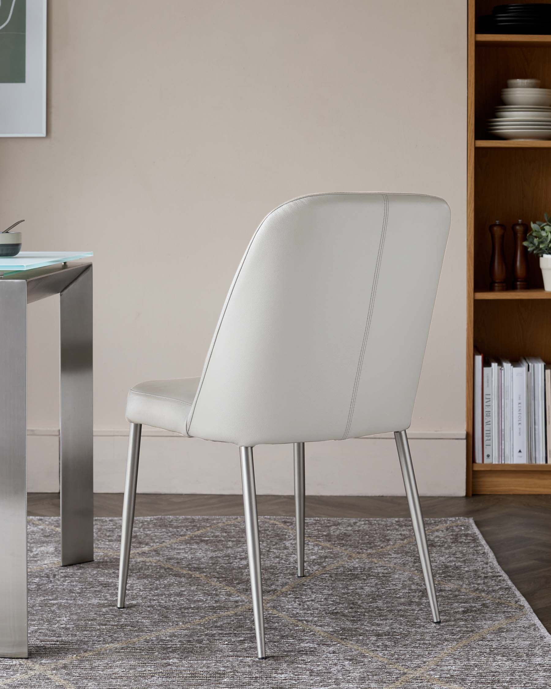 A sleek, modern white dining chair with metal legs, positioned beside a glass-top table and a wood shelf in a stylish room.