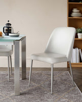 A modern dining set featuring a sleek glass-top table and minimalist white chairs with metal legs, set on a patterned rug.