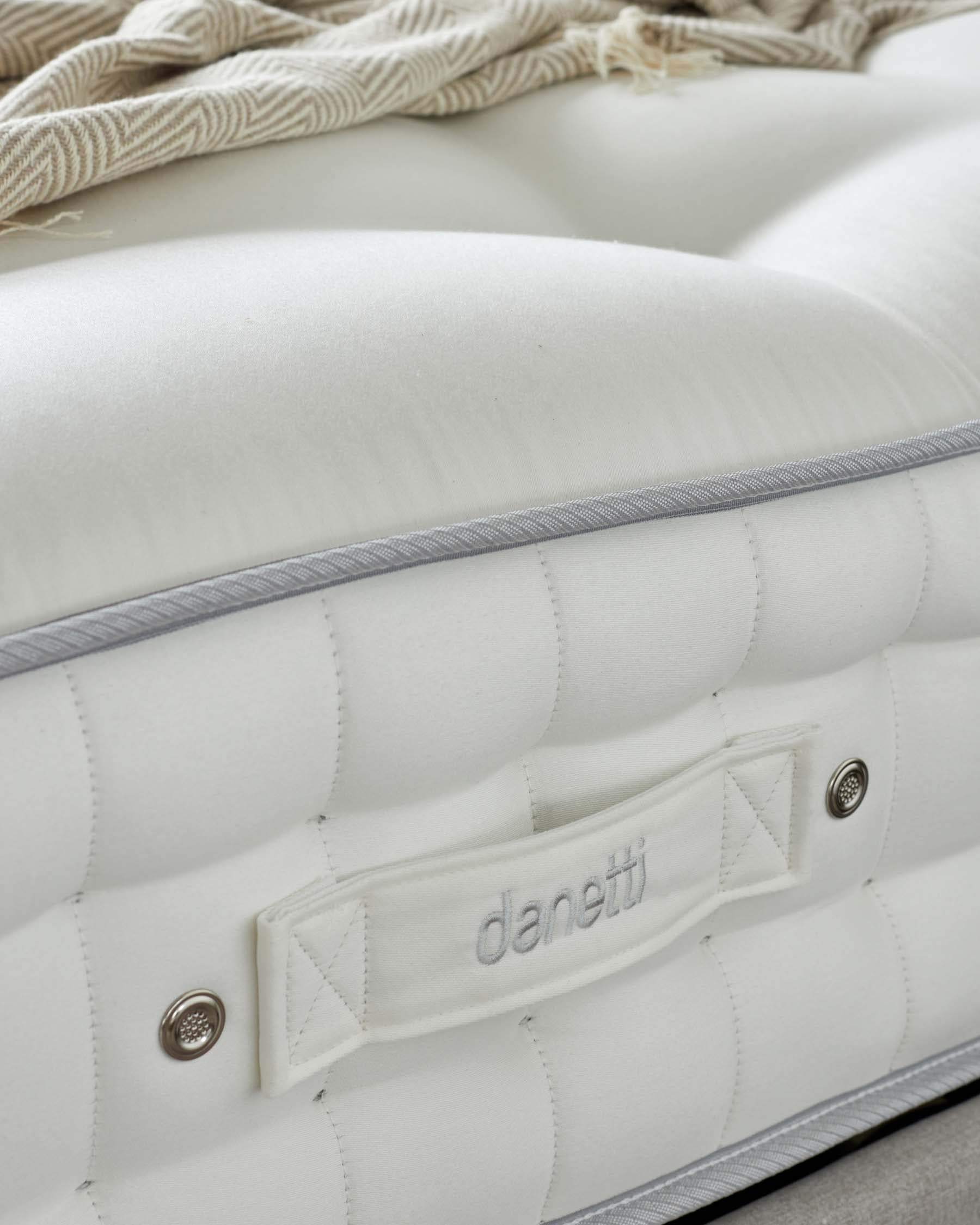 Close-up of a plush, white mattress with tufted detailing and a silver trim, complemented by a soft patterned throw blanket.