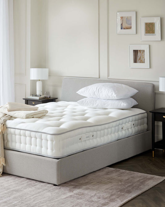 A plush mattress with a light gray upholstered base, accented by white bedding, paired with sleek nightstands and lamps.