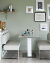 Modern minimalist dining set featuring a square white tabletop with a single pedestal base paired with two sleek white leather benches with chrome legs and frame.