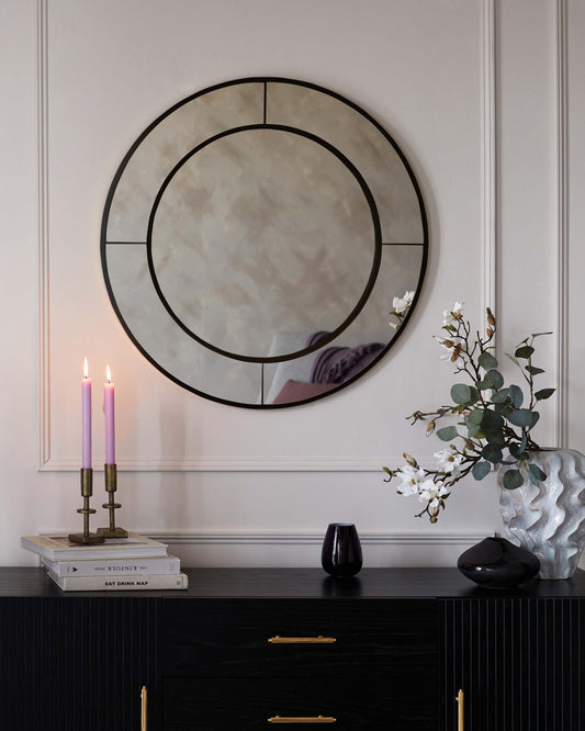 Elegant black wooden sideboard with ribbed front panels and brass handles, topped with a selection of decorative items including books, a candle holder, and vases.