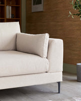 Beige modern sofa with plush cushions and minimalistic black metal legs, placed against a textured brown wall with decorative elements.