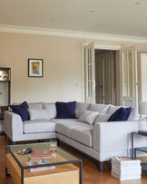 A light gray sectional sofa with navy cushions, a glass-top coffee table, and a side table with magazines and decor.