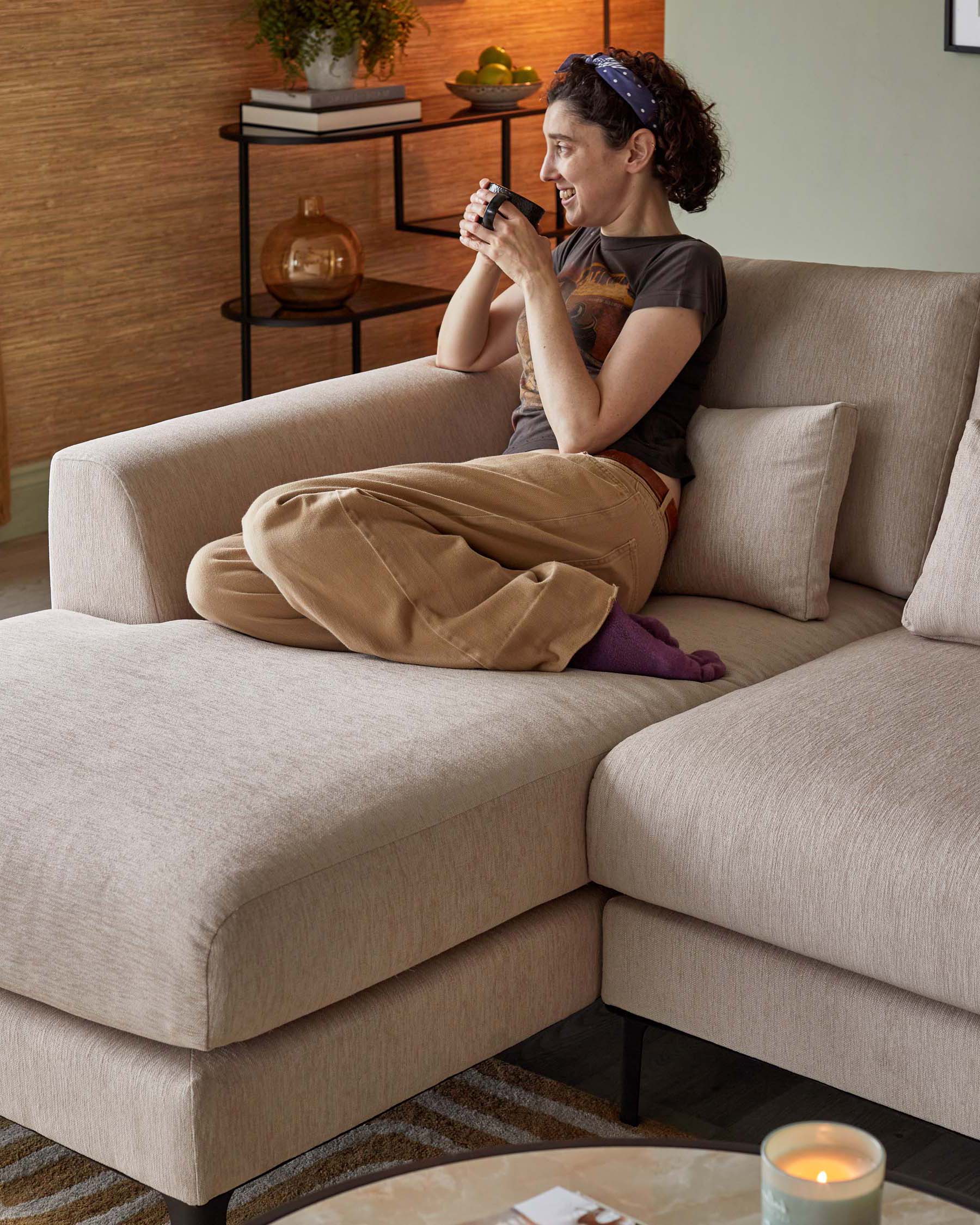 A contemporary beige fabric sectional sofa with plush back cushions and a sleek wooden bookshelf in the background with decorative items on the shelves.