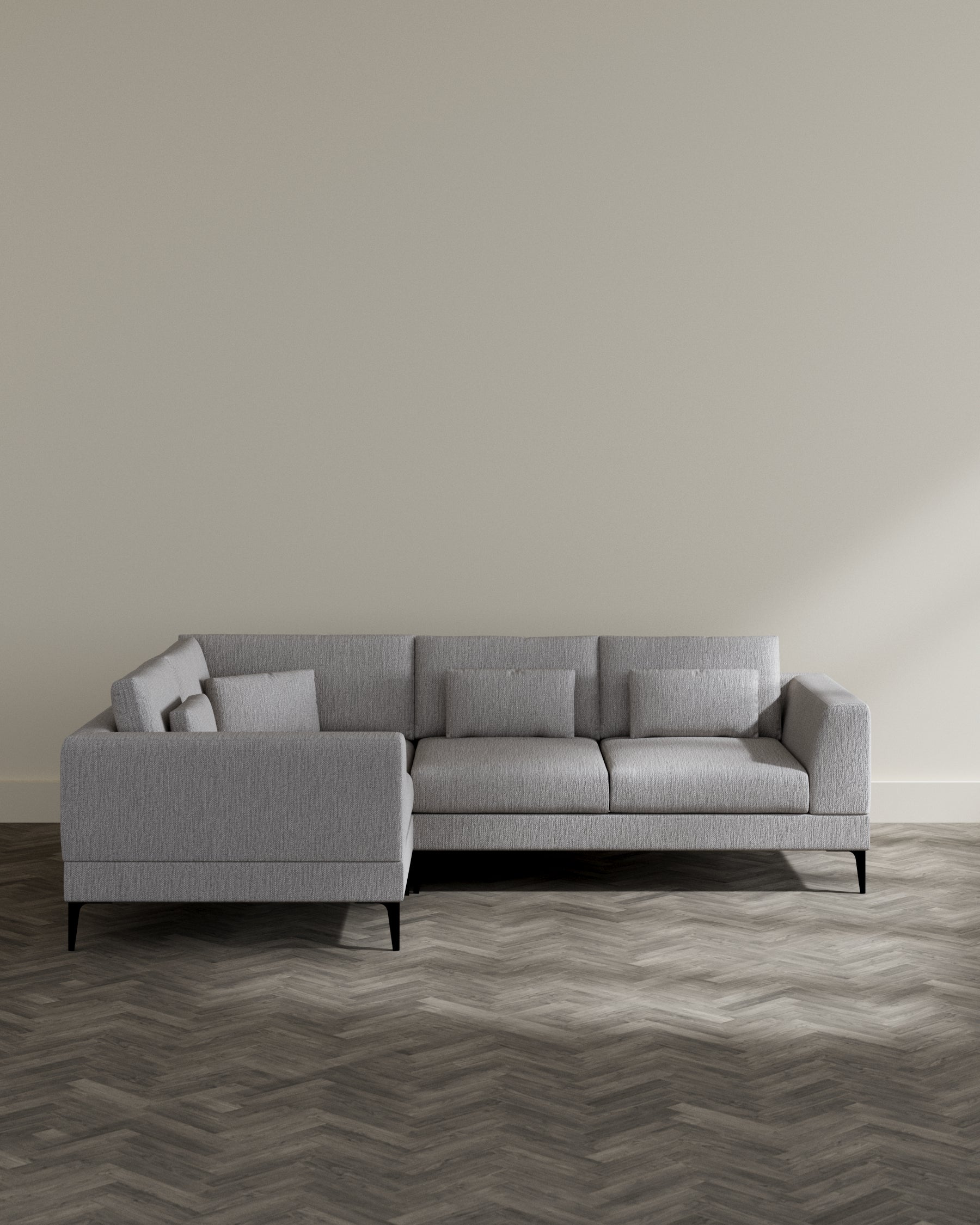 Modern light grey fabric sectional sofa with simple lines, three seat cushions, and two matching rectangular throw pillows, elevated on dark wooden legs, set in a minimalist room with herringbone-patterned wood flooring.