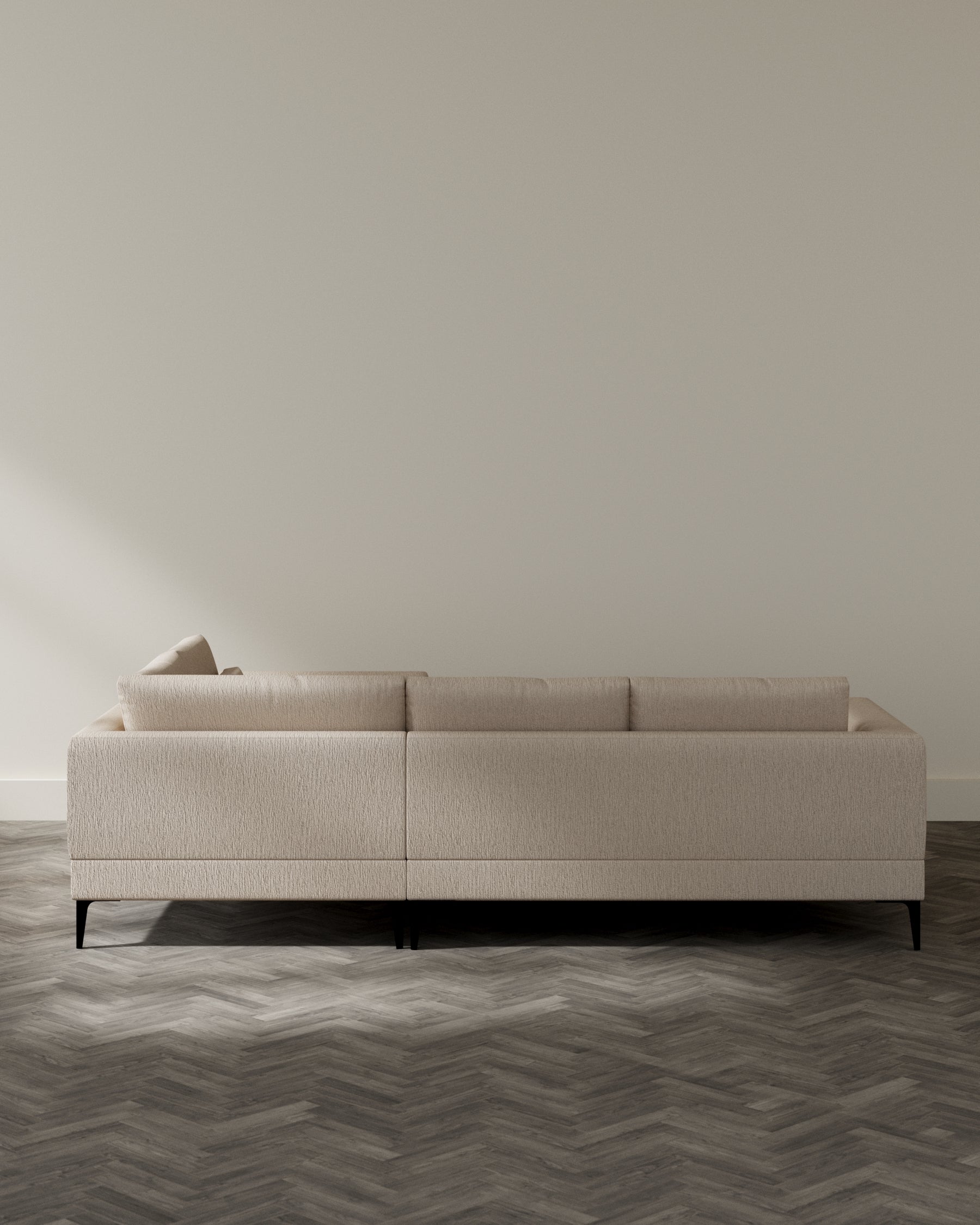 Contemporary beige fabric sofa with clean lines and minimalist design, featuring plush back cushions and a sturdy dark wooden leg base, set in a room with herringbone-patterned wooden flooring and neutral walls.