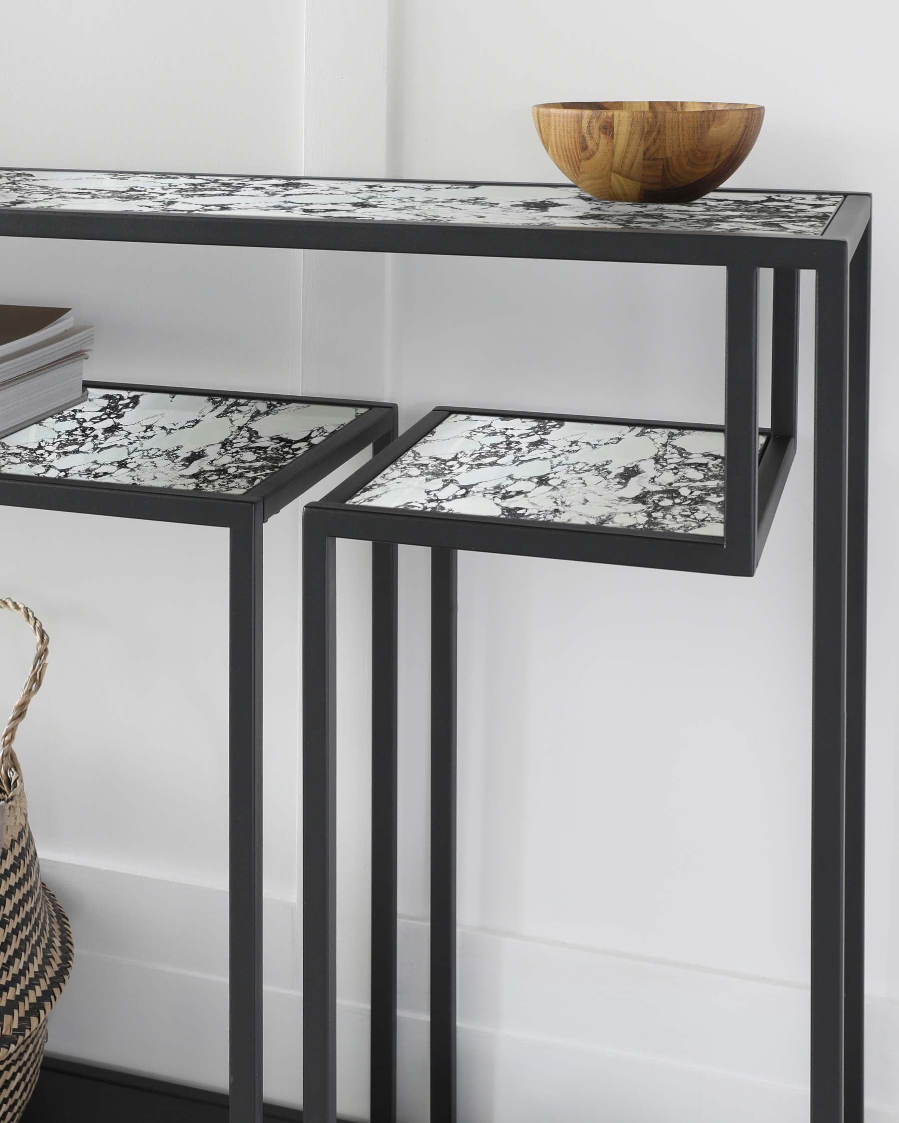 Black metal console table with marble-patterned tops and a wooden bowl, complemented by a woven basket.