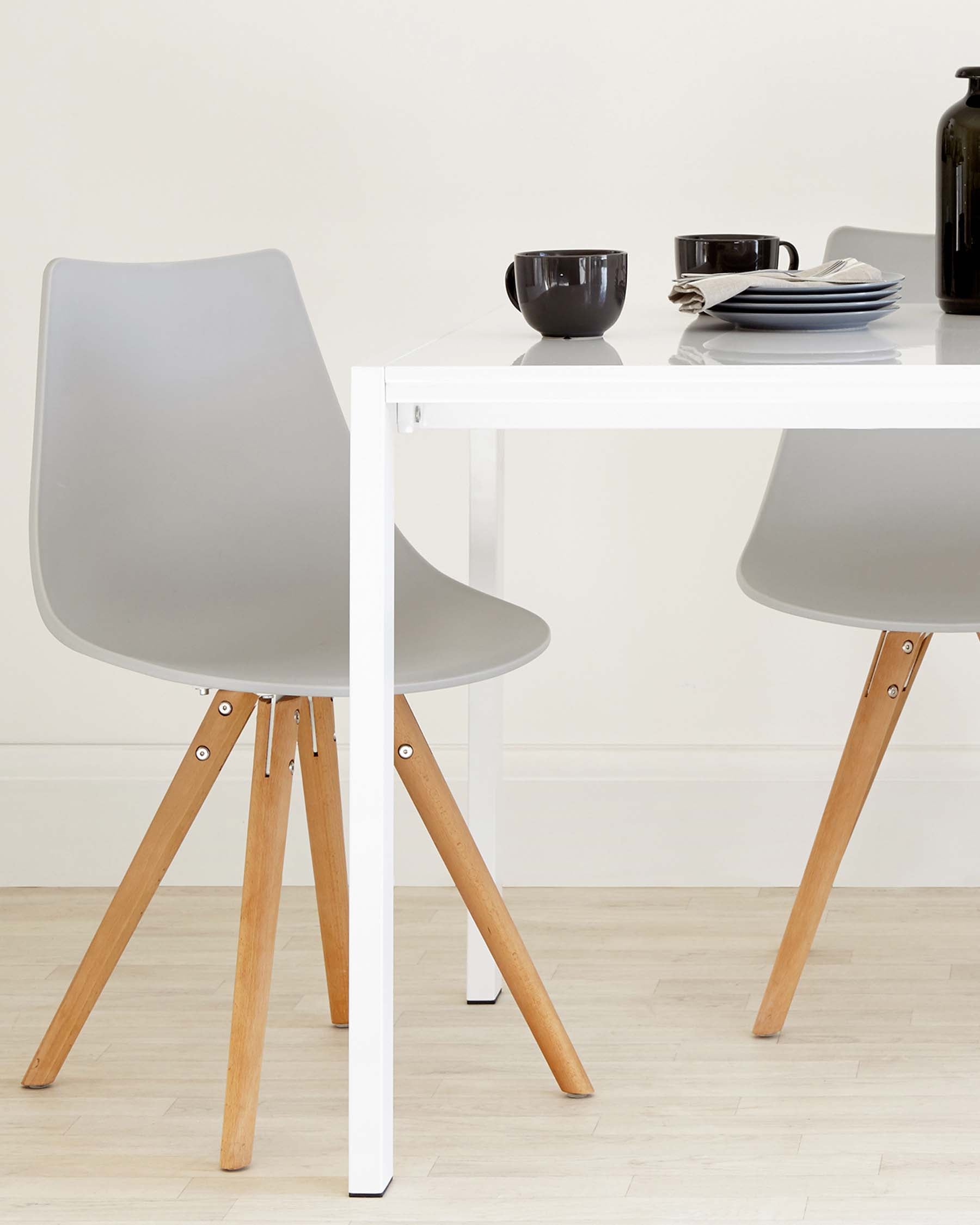 Modern dining setup featuring a sleek white table, two gray chairs with wooden legs, and minimalist dishware.