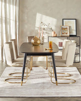 A contemporary dining room setup featuring a round, dark wood table with a fluted design and elegant brass-coloured metal legs. Four matching modern chairs with cream upholstery and brass legs are arranged around the table. The table and chairs are set on a white textured area rug. A coordinating console table with a metal frame and a glass top displays decorative items and is placed against the wall.