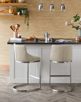 Two modern beige barstools with sleek chrome bases, paired with a dark countertop and minimalistic kitchen accessories.